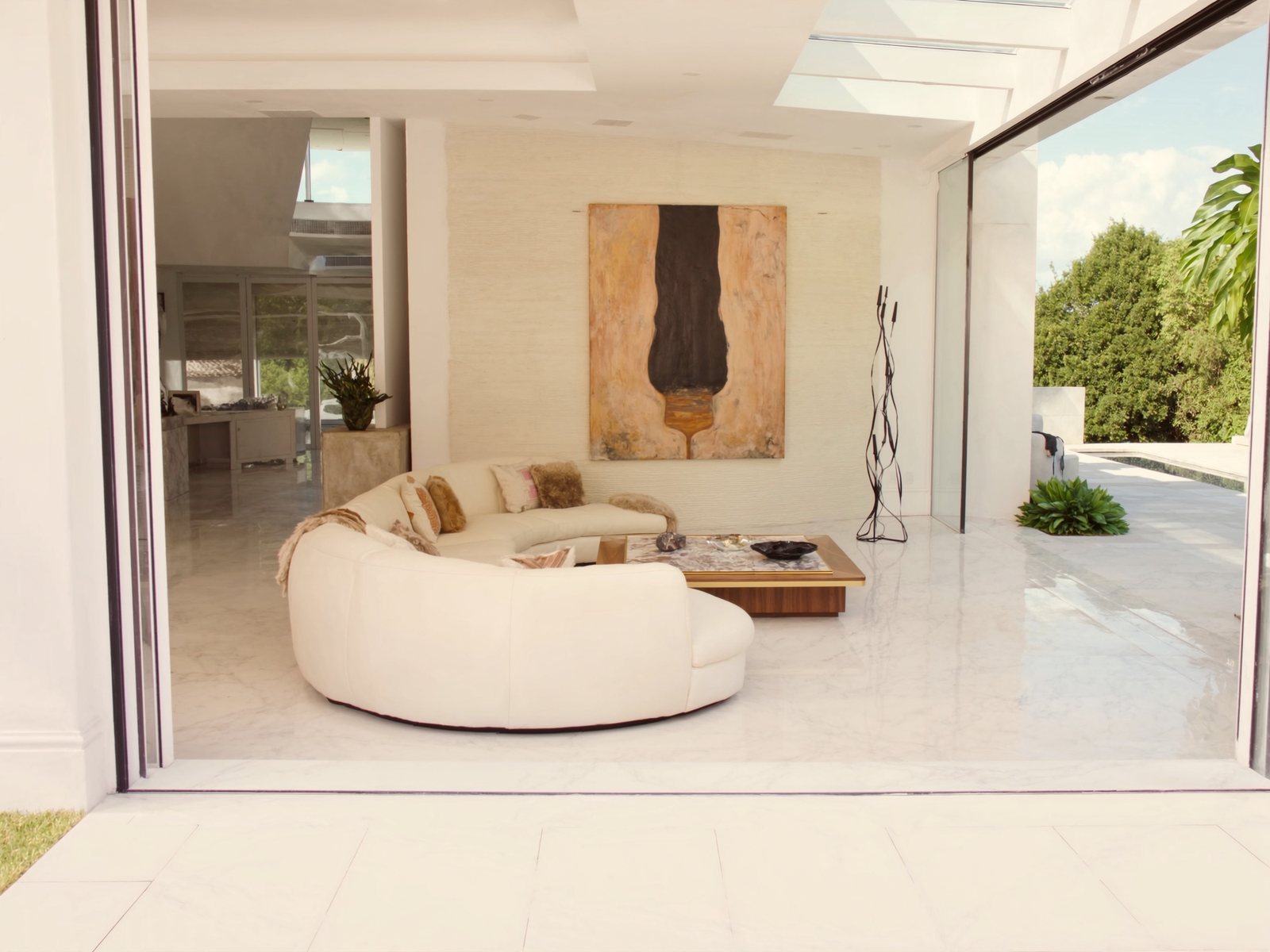 Sun-filled luxury living room in a Boca Raton estate featuring a cream bouclé sectional, walnut coffee table, and floor-to-ceiling sliders opening to a tropical pool deck