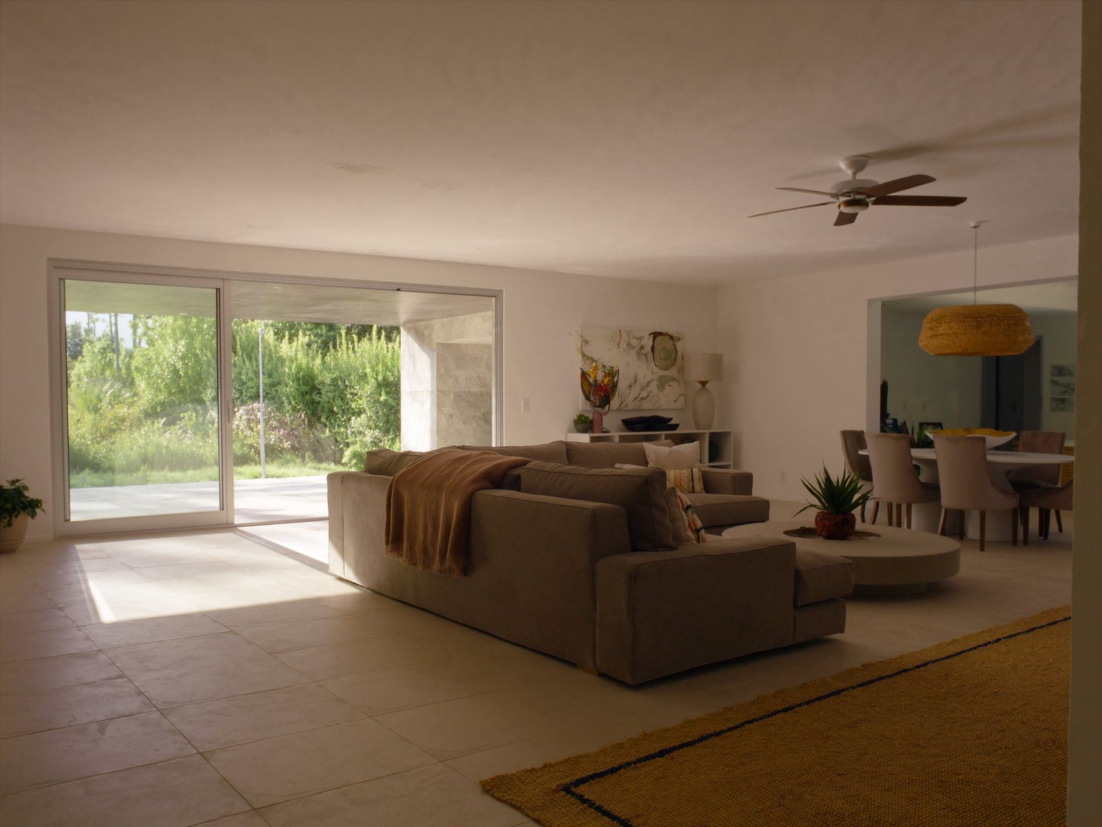 Bright open-plan family living and dining room in a Coral Springs home, featuring a large greige sectional, wood-look tile floors, and natural South Florida light