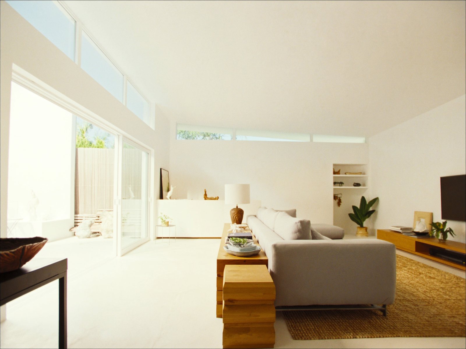 Bright South Florida living room with a light-gray fabric sectional, woven jute rug, and tropical plants in natural afternoon light