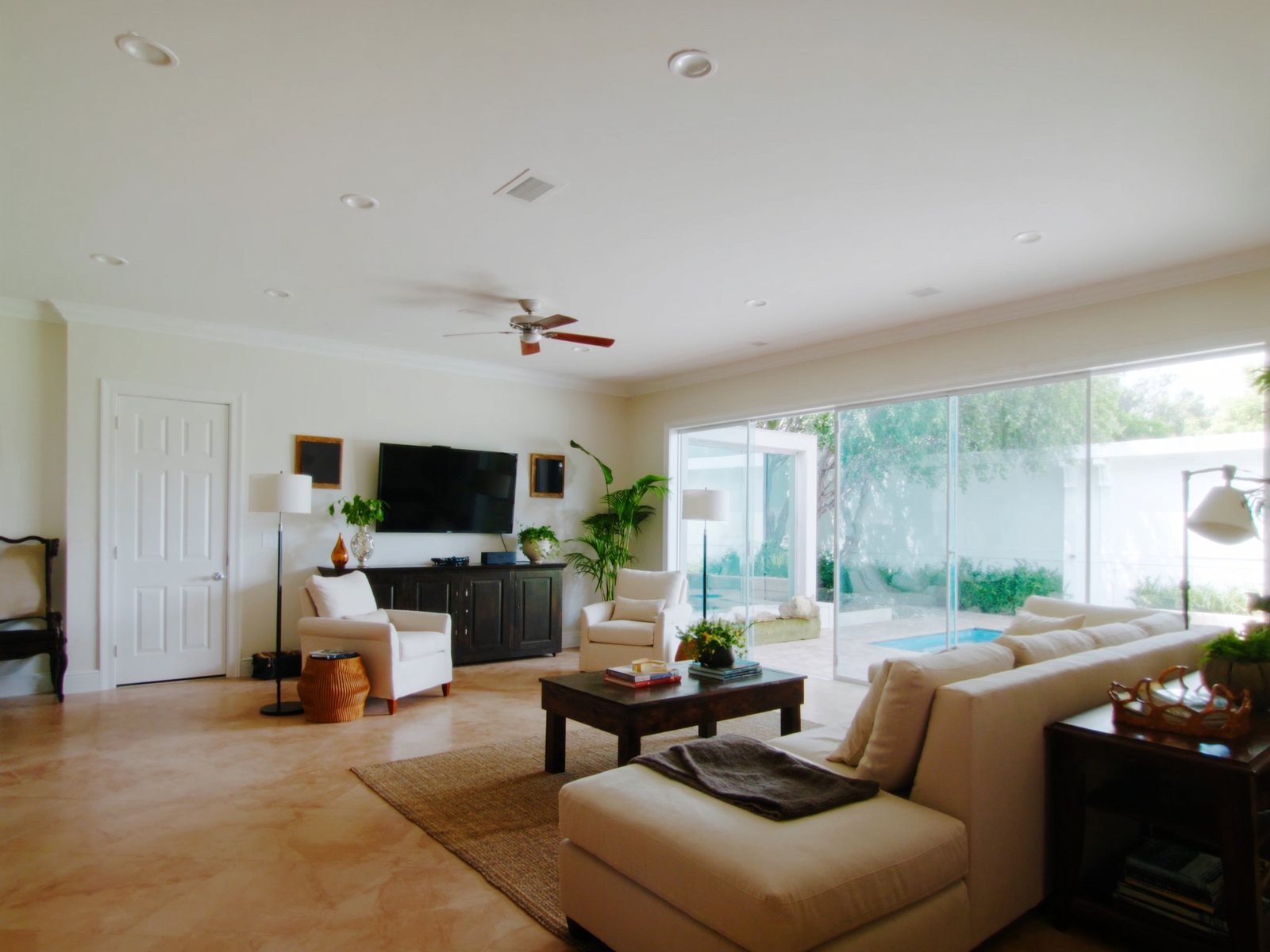 Bright open-plan vacation rental living room in Orlando, Florida, with a neutral fabric sectional, sliding glass doors to a screened pool lanai, and warm natural Florida afternoon light