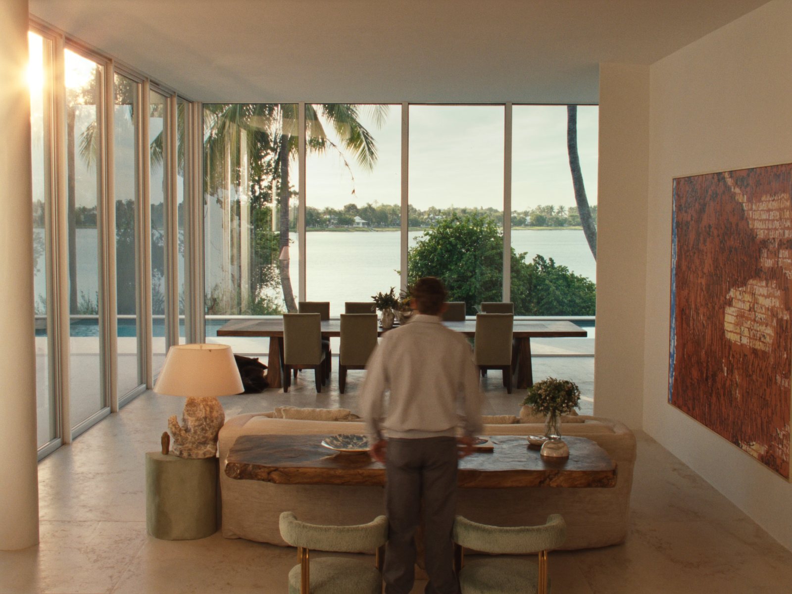 Coastal estate living and dining room in Sarasota, Florida with curved linen sofa, boucle accent chairs, smoked oak dining table, and floor-to-ceiling bay views in warm morning light