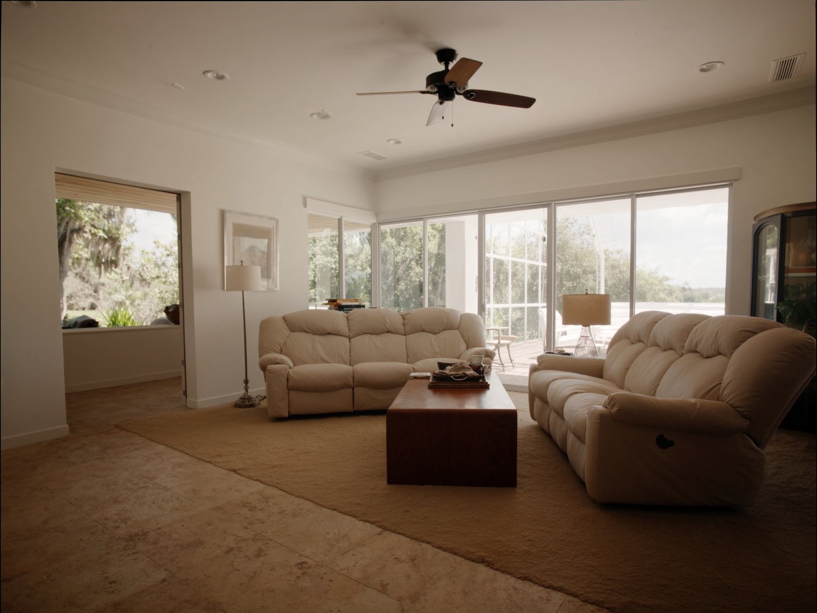 Sun-filled retirement villa living room with cream recliner sofa set, walnut coffee table, and warm natural light from screened lanai doors
